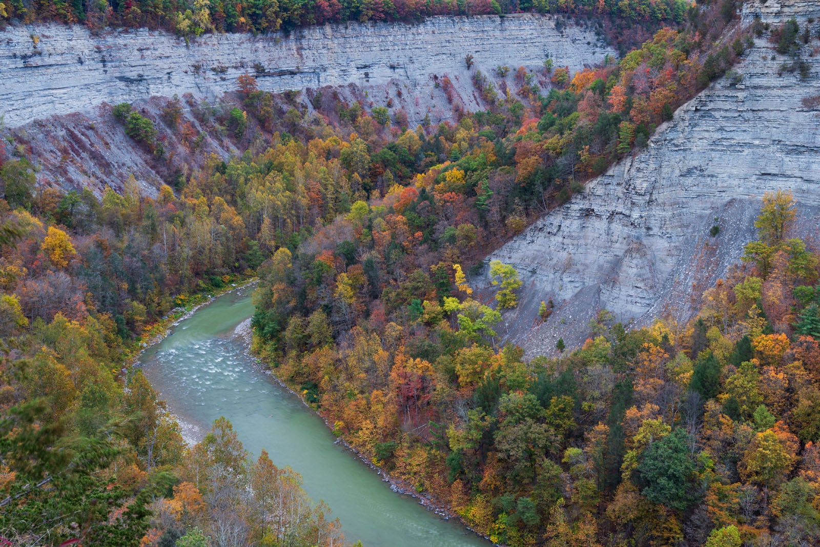A winding river flows between steep, rocky cliffs covered in vibrant autumn trees with red, orange, and yellow foliage.