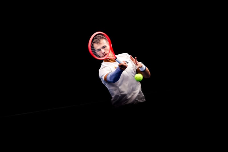 A tennis player in a white shirt and blue wristbands is focused as he reaches forward to hit a green tennis ball with his red racket against a black background.
