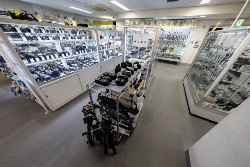 A well-lit camera store interior with glass display cases and shelves filled with cameras, lenses, and photography equipment, arranged neatly throughout the shop.