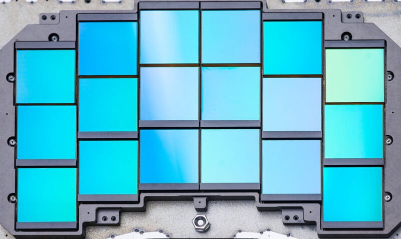 A close-up view of a rectangular array of blue-green reflective glass or semiconductor panels arranged in a black metal frame, resembling a microchip or photonic device.