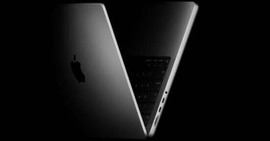 A partially open silver MacBook viewed from the side, showing the Apple logo on the lid, part of the keyboard, and several ports along the edge, set against a black background.