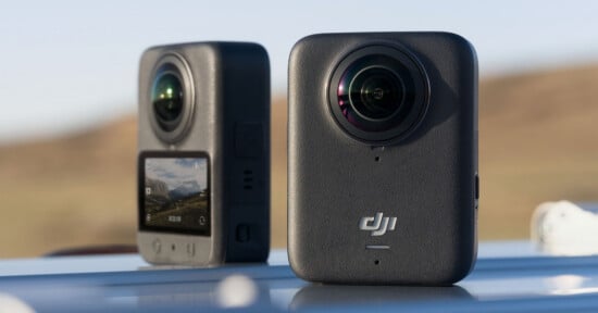 Two gray DJI 360-degree action cameras are positioned on a reflective surface outdoors, one showing its front lens and logo, the other displaying its rear screen with a landscape image.