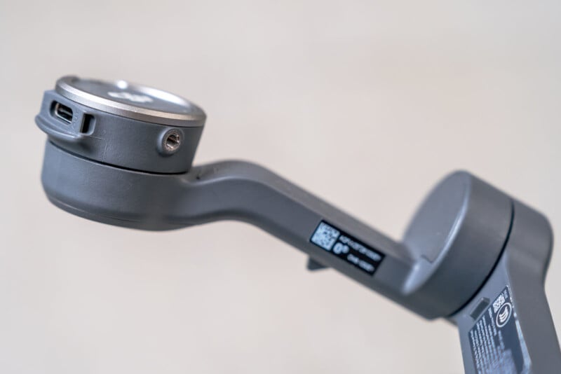 A close-up of a gray gimbal arm with a visible USB-C port and QR code on a neutral background.