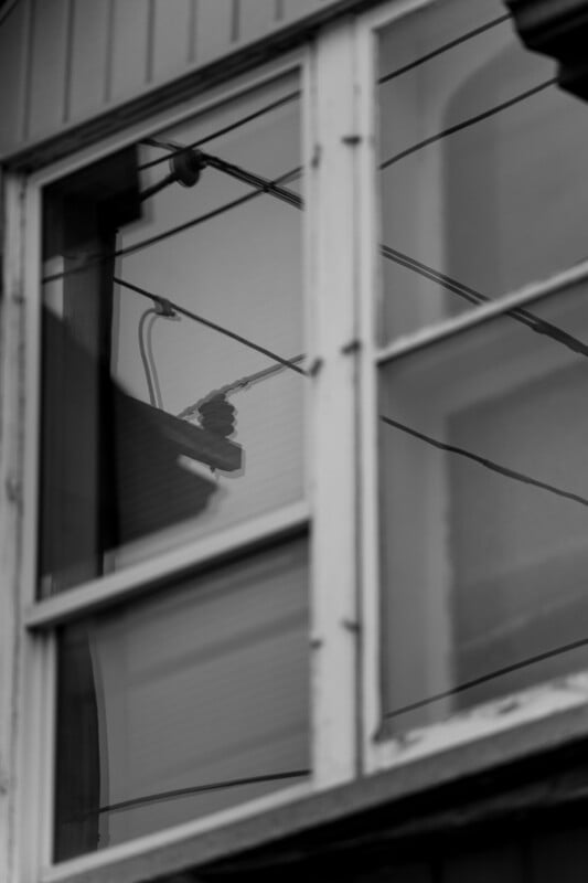 Black and white photo of a window with four glass panes, reflecting overhead power lines and a street lamp. The image is slightly blurred, creating a moody and abstract atmosphere.