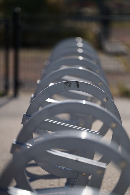 A close-up, angled view of an empty metal bike rack outdoors, with circular loops creating a repeating pattern, and a blurred background.