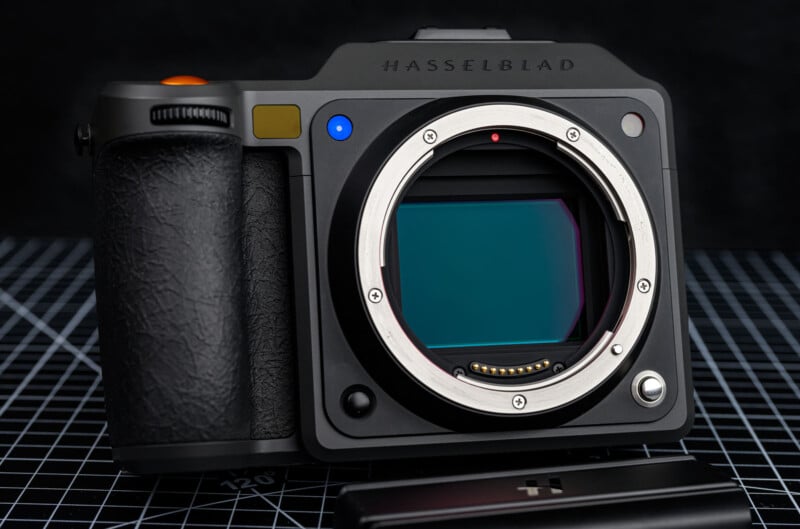 A close-up of a Hasselblad digital camera body without a lens, showing the sensor and control buttons, resting on a black grid-patterned surface.