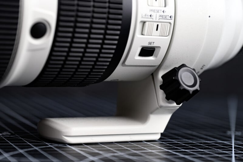 Close-up of a white telephoto camera lens with focus and preset switches, mounted on a tripod collar, resting on a grid-patterned surface.