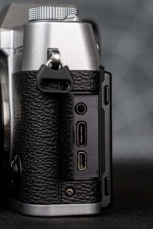 Close-up of the side of a silver and black digital camera showing three open ports: a headphone jack, a HDMI port, and a USB port, with the rubber port cover folded back.