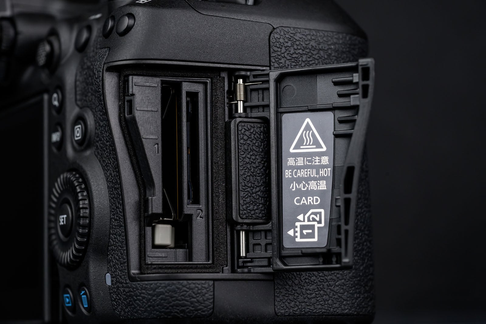 Close-up of an open DSLR camera memory card slot, revealing two card slots labeled 1 and 2. The door has a warning label in English and Chinese about high temperature and handling cards carefully.
