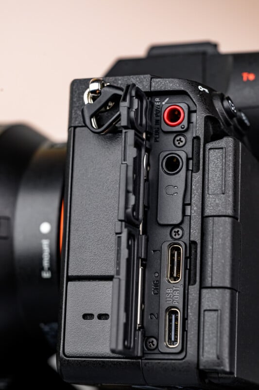 Close-up of a digital camera’s side panel showing various ports, including two SD card slots, USB, HDMI, headphone, and microphone jacks, with protective covers open.