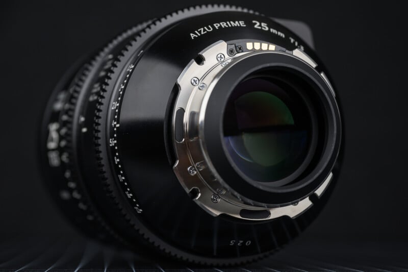Close-up view of a camera lens labeled "Aizu Prime 25mm," highlighting the polished metal mount and glass elements, set against a dark background.