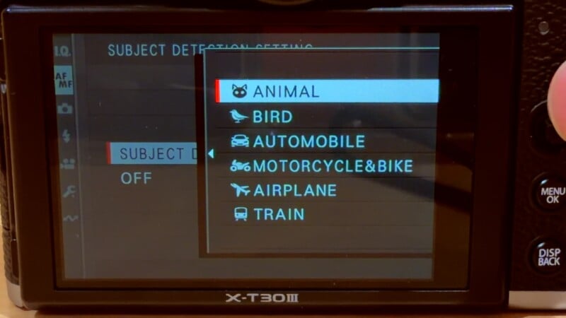A digital camera screen displays a menu with subject detection settings, highlighting options including Animal, Bird, Automobile, Motorcycle & Bike, Airplane, and Train. The Animal option is currently selected.