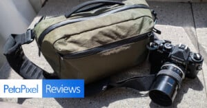 A green camera bag and a vintage Nikon film camera with a lens rest on a concrete surface. The lower left corner displays the "PetaPixel Reviews" logo.