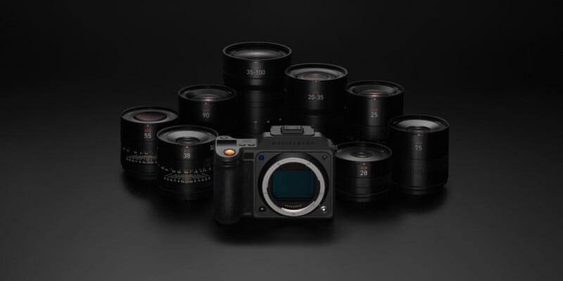 A digital camera body with eight different camera lenses arranged in a semicircle behind it, all displayed on a dark surface with a black background.