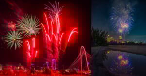 A vibrant fireworks display in a city skyline. On the left, multicolored fireworks illuminate a bridge and buildings with emphasis on red trails. On the right, blue and white fireworks burst against the night sky, reflected on a wet surface below.