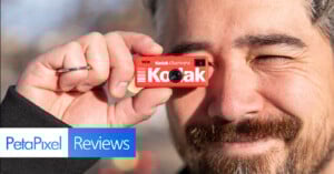 A smiling man holds a tiny red Kodak camera up to his eye as if taking a photo. The image includes "PetaPixel Reviews" text in the bottom left corner.