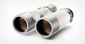 A pair of sleek, modern white binoculars with metallic accents is shown on a light background, viewed from an angle that highlights the lenses and textured surface.
