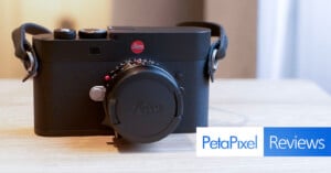 A black Leica camera with a lens cap is placed on a light wooden surface. The image features the "PetaPixel Reviews" logo in the bottom right corner.