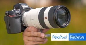A hand holds a Nikon camera body attached to a large white Sony G Master zoom lens with a blurred outdoor background. The image includes the Petapixel Reviews logo in the lower right corner.