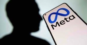 A smartphone screen displays the Meta logo and text, with the blurred silhouette of a person in the background.