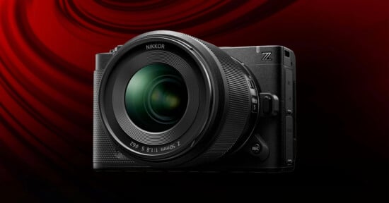 A black Nikon Z series digital camera with a large NIKKOR lens is displayed against a dark red, swirling background.