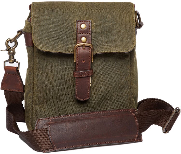 An olive green canvas crossbody bag with a front flap secured by a brown leather strap and brass buckle, featuring an adjustable shoulder strap with a leather pad.