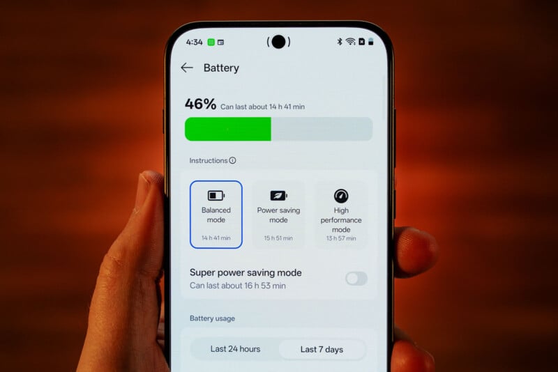 A hand holds a smartphone displaying the battery settings screen, showing 46% battery remaining with options for balanced, power saving, and high performance modes.