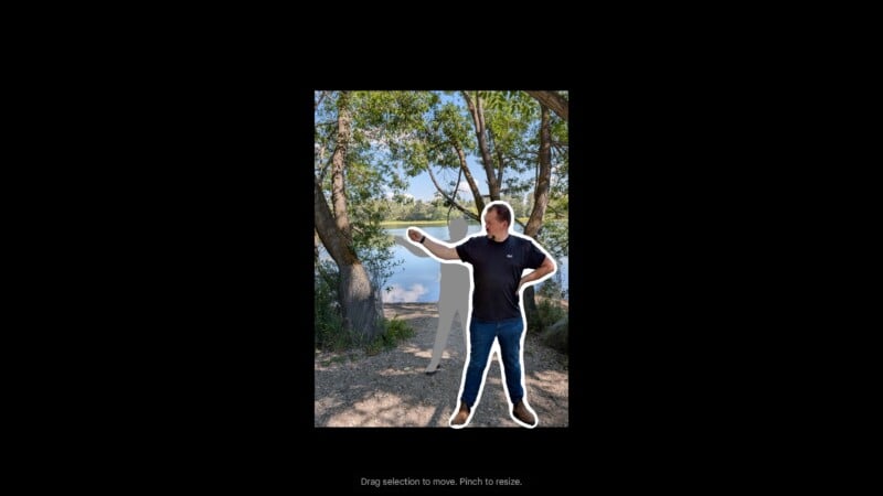 A person in a black shirt and jeans stands outdoors near trees and a body of water, outlined with a white border. A faded silhouette of the person is behind them, suggesting they were digitally moved in the image.