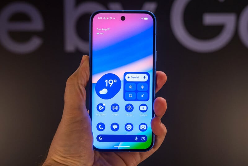 A hand holds a smartphone displaying a colorful home screen with weather, app icons, and widgets. The background is blurred and dark, highlighting the phone’s bright display.