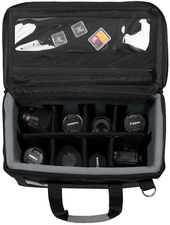 A camera bag with open top, showing organized compartments holding camera lenses, a camera body, and SD memory cards stored in a clear zippered pocket on the inner lid.