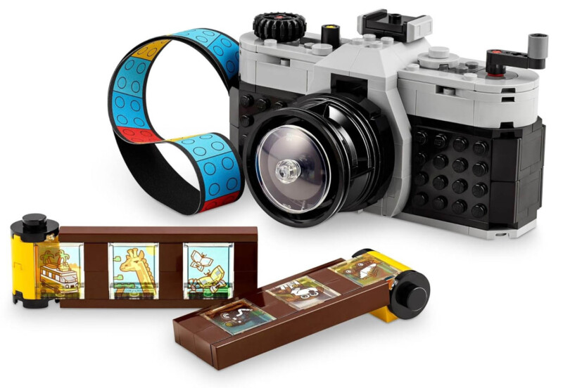 A toy camera built from LEGO bricks, with a colorful strap and two film strips featuring cartoon animal scenes, including a giraffe and a monkey.