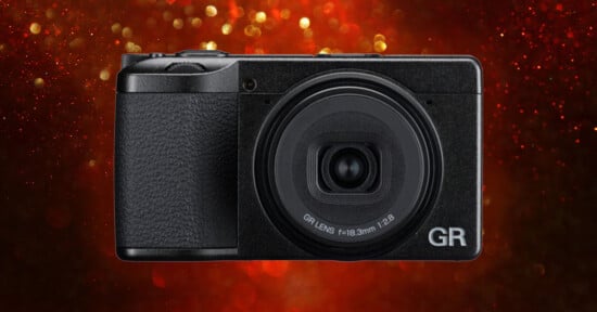 A black compact digital camera with a GR lens is centered against a red background with glowing bokeh lights.