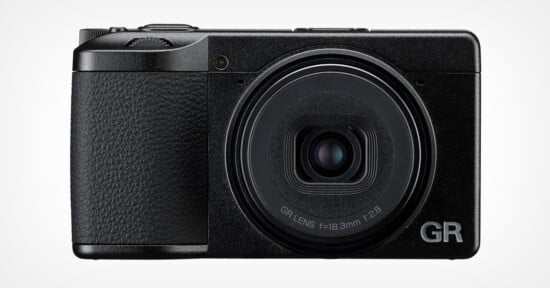 A compact black digital camera with a textured grip, prominent fixed lens, and the letters "GR" in silver on the bottom right corner of the front panel.