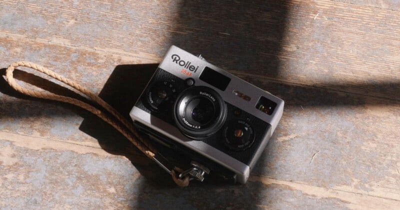 A vintage Rollei 35 AF film camera with a wrist strap lies on a wooden floor, partially lit by sunlight streaming through a window.