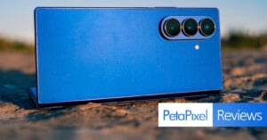 A blue smartphone with three rear cameras laying on a textured outdoor surface, with the "PetaPixel Reviews" logo overlaid in the bottom right corner.