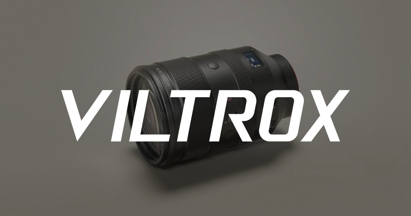 A black camera lens lies on a light gray surface with the word "VILTROX" in large, bold white letters displayed across the image.