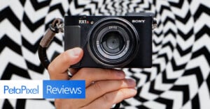 A hand holding a Sony RX1R camera in front of a black and white zigzag patterned background, with "PetaPixel Reviews" text logo overlay at the bottom left.