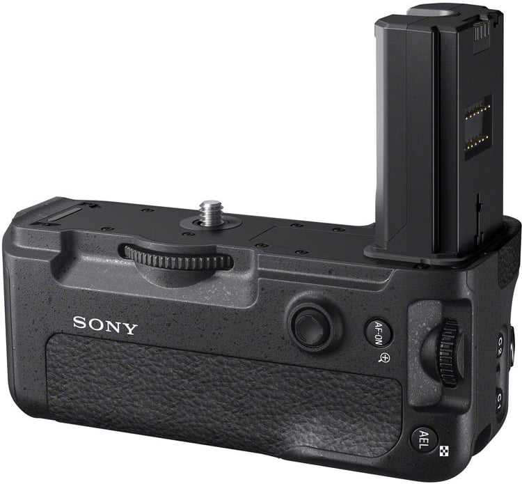 A black Sony camera battery grip with a textured surface, multiple buttons, dials, and a partially inserted battery on the top right side.