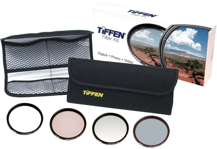 A Tiffen filter kit with a black carrying case, mesh pouch, product box, and four different camera lens filters arranged in a row in front of the case.