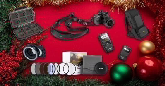 A festive holiday background with pine branches, baubles, and berries displaying camera accessories: memory card case, camera, lens adapter, filters, camera strap, remote controls, and a backpack.