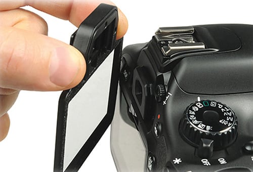 A hand is flipping out the LCD screen of a black DSLR camera, showing the camera's buttons, dials, and controls up close.