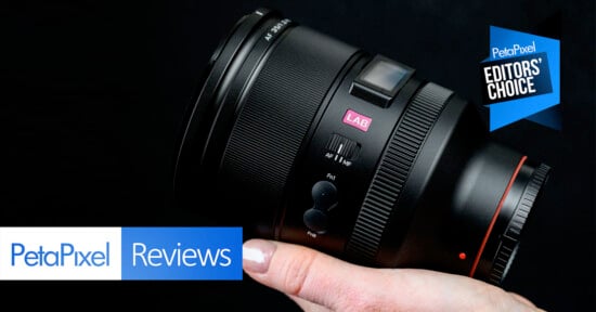 A hand holding a camera lens against a dark background, with Petapixel Reviews and Editors' Choice badges displayed in the image corners.