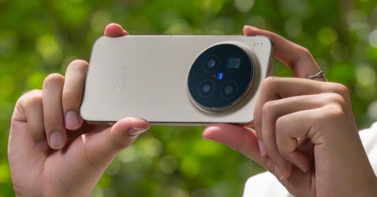 A person holds a gold Vivo smartphone horizontally, focusing on its large circular triple camera module, with a green leafy background blurred behind.