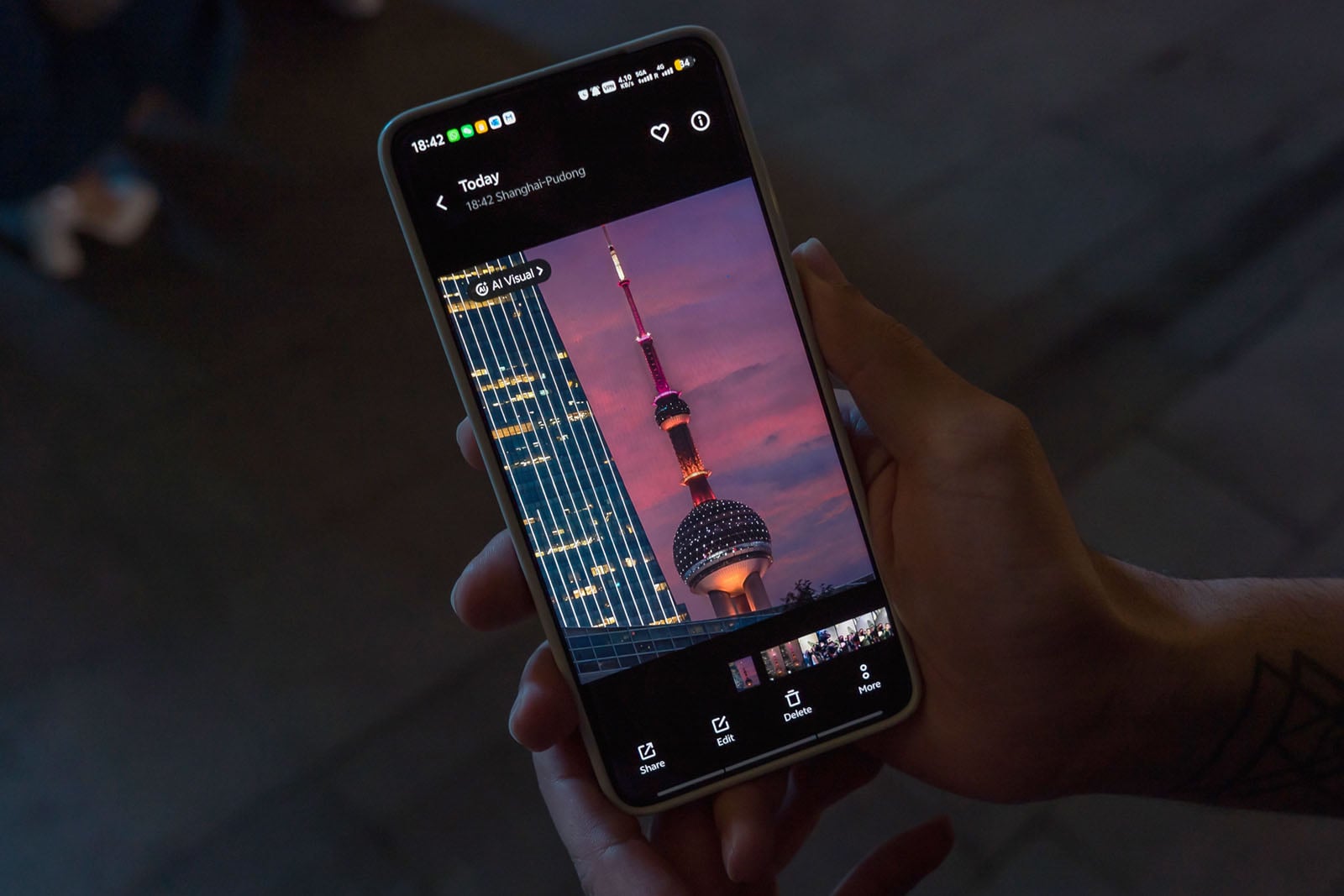 A person holds a smartphone displaying a photo of Shanghai’s Oriental Pearl Tower at sunset, with city lights and a tall building beside it. The phone screen shows various editing and sharing options.