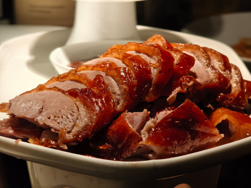 Slices of roasted duck with crispy, golden-brown skin and tender meat are neatly arranged on a white plate, ready to be served.